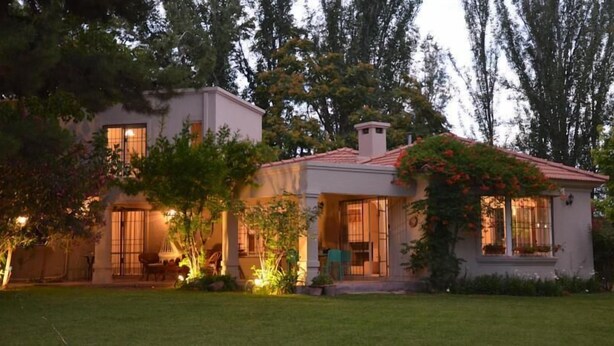 A two-story house with a patio, surrounded by trees and a well-maintained lawn. - Angelo di Caneva (Chacras de Coria)