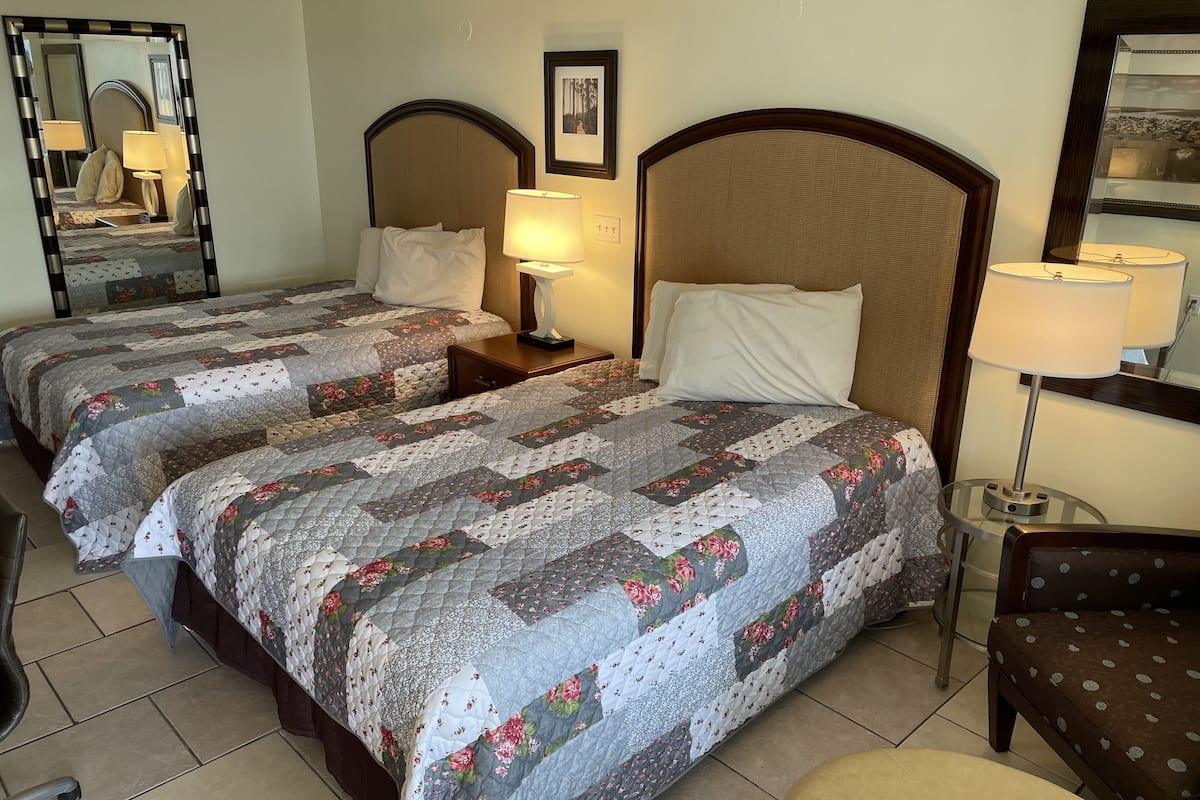 A hotel room with two beds, each with a floral quilt, bedside lamps, and a large mirror on the wall.