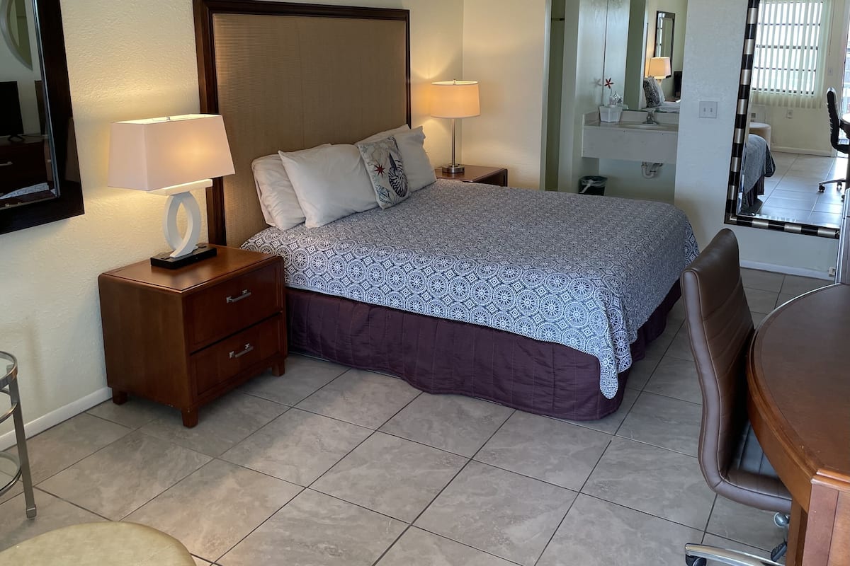 A hotel room with a large bed, two bedside tables, a chair, a desk, and a mirror.