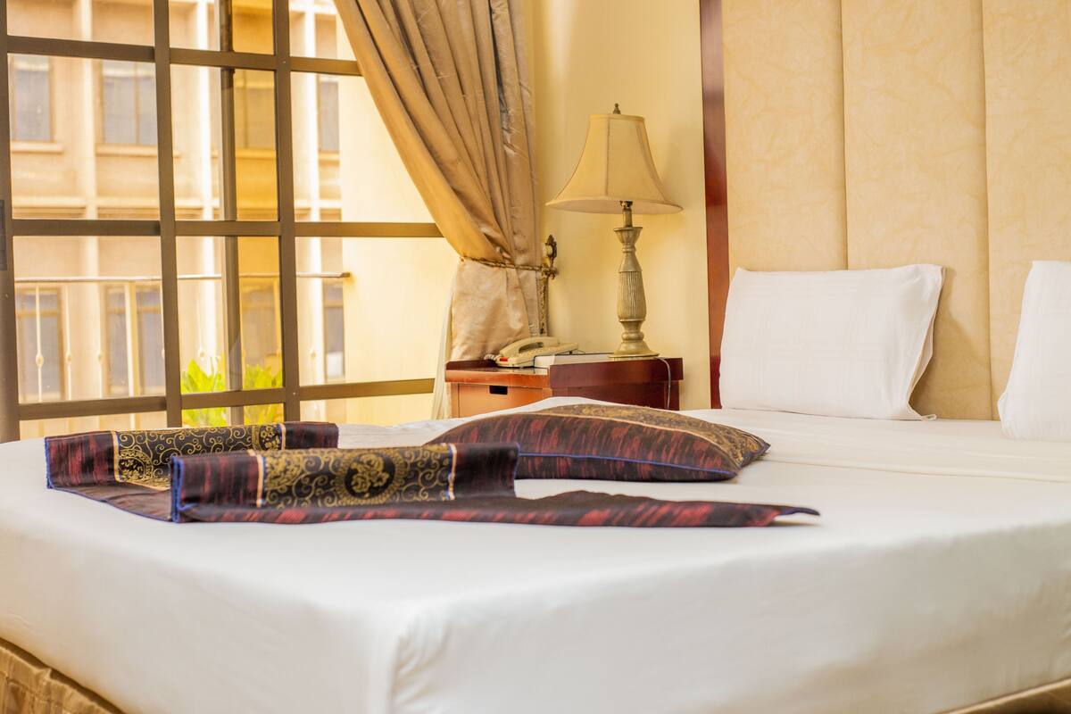 Una habitación de hotel con una cama, una mesita de noche, una lámpara y una ventana con cortinas.