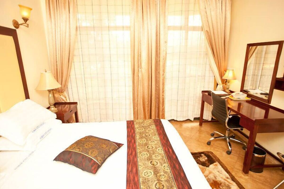 Una habitación de hotel con una cama, un escritorio, una silla, una lámpara y un espejo.