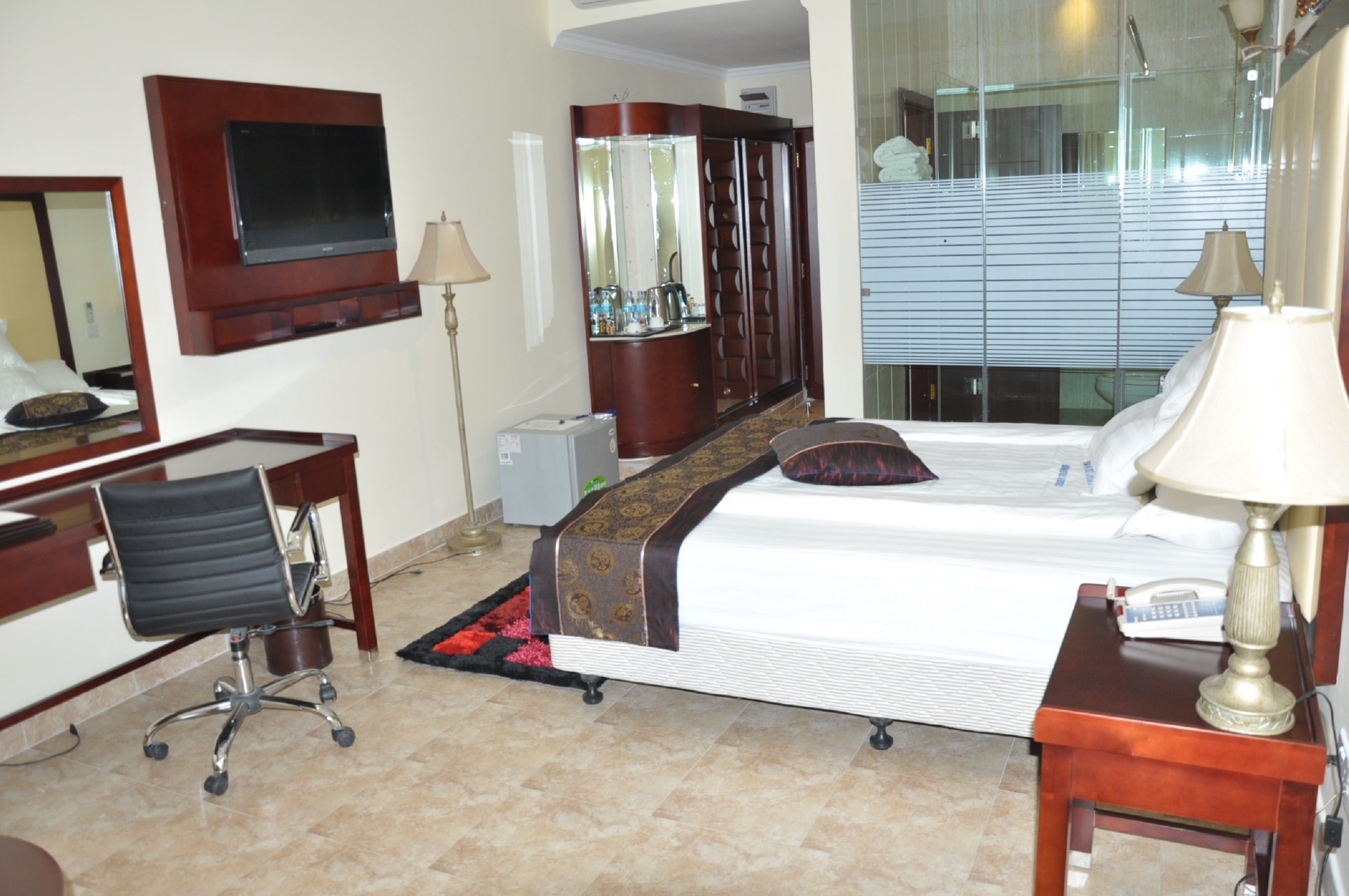 A hotel room with a bed, desk, chair, TV, wardrobe, and a mirror.