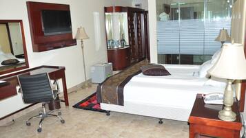 A hotel room with a bed, desk, chair, TV, wardrobe, and a mirror.