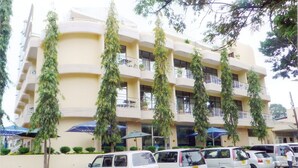 A multi-story hotel with a beige facade, balconies, and parked cars in the foreground. - Nyumbani Hotels & Resorts - Moshi (Moshi)