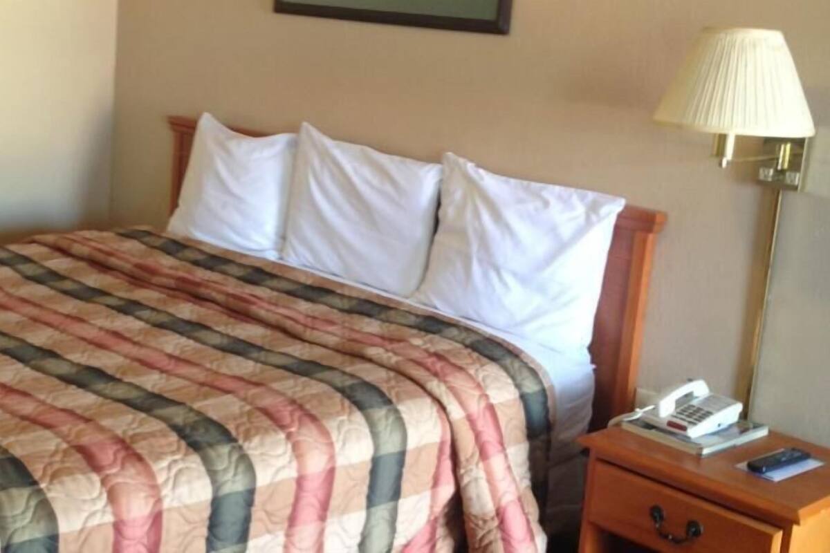 A neatly made bed with a striped bedspread, a bedside lamp, and a nightstand with a book and a remote control.
