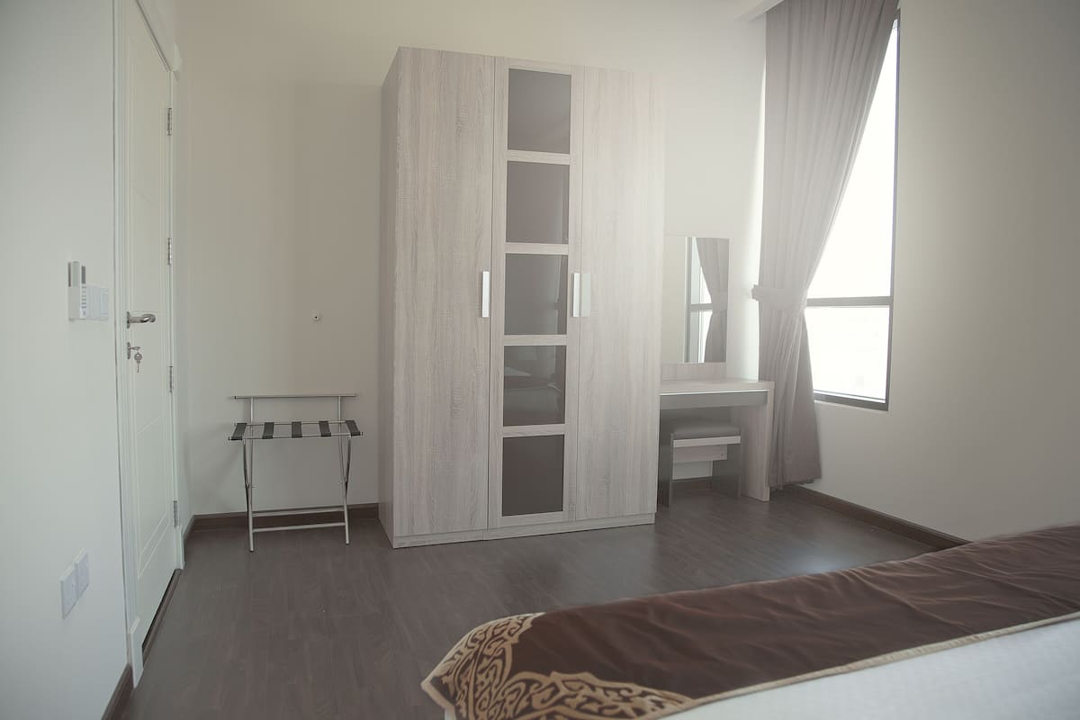 Une chambre à coucher comprenant une armoire, une table de chevet, un lit et une fenêtre avec des rideaux.