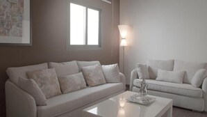 A modern living room with two white sofas, a glass coffee table, a floor lamp, and a window providing natural light. - Rafa Homes  (Riyadh)
