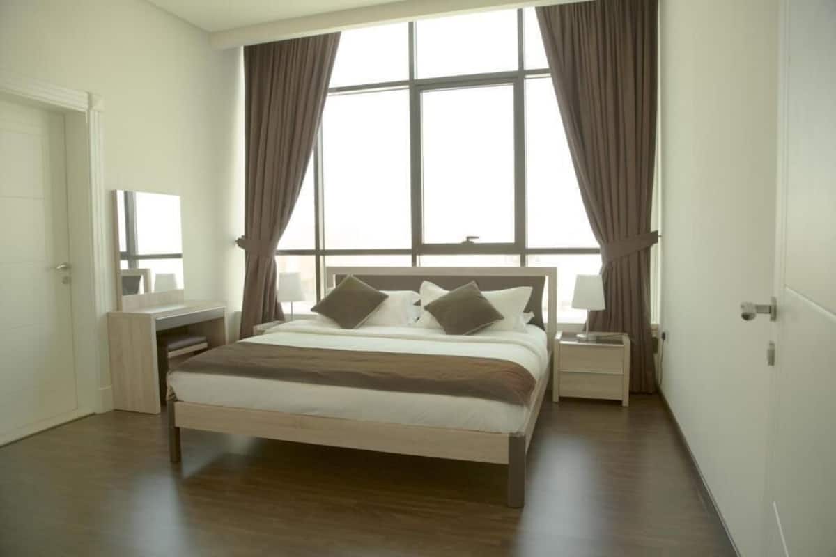 Une chambre à coucher comprenant un lit, des tables de chevet, un bureau et une grande fenêtre avec des rideaux.