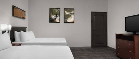 Une chambre d’hôtel avec deux lits, une commode, un téléviseur et deux tableaux encadrés au mur.