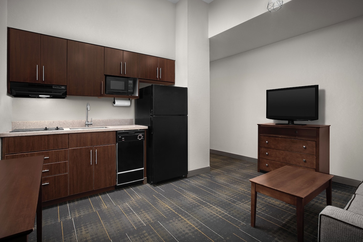 Una cocina moderna con alacenas de madera oscura, un refrigerador negro, un microondas y un televisor de pantalla plana sobre un pedestal de madera.