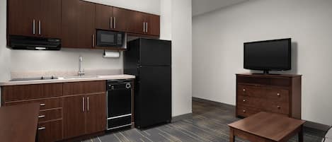 A modern kitchen with dark wood cabinets, a black refrigerator, a microwave, and a flat-screen TV on a wooden stand.