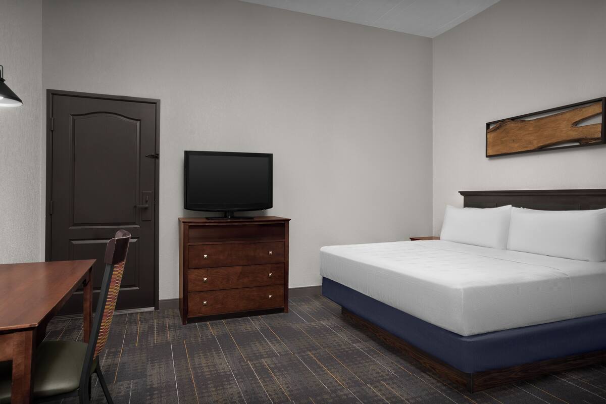 A hotel room with a bed, a TV on a dresser, a chair, and a wooden headboard.
