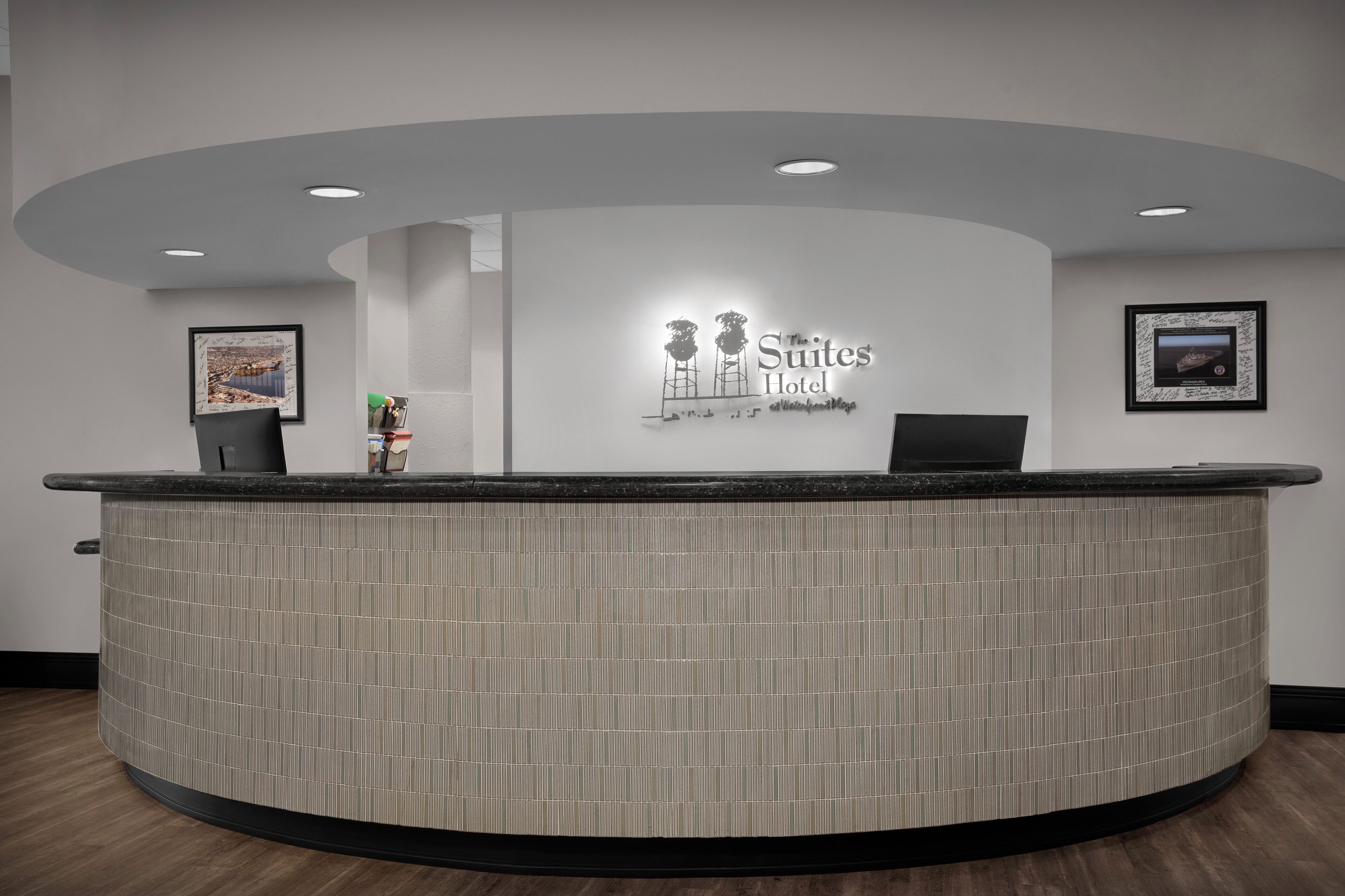 A reception desk with a tiled design, a framed picture on the wall, and a sign for 'The Suites Hotel'.