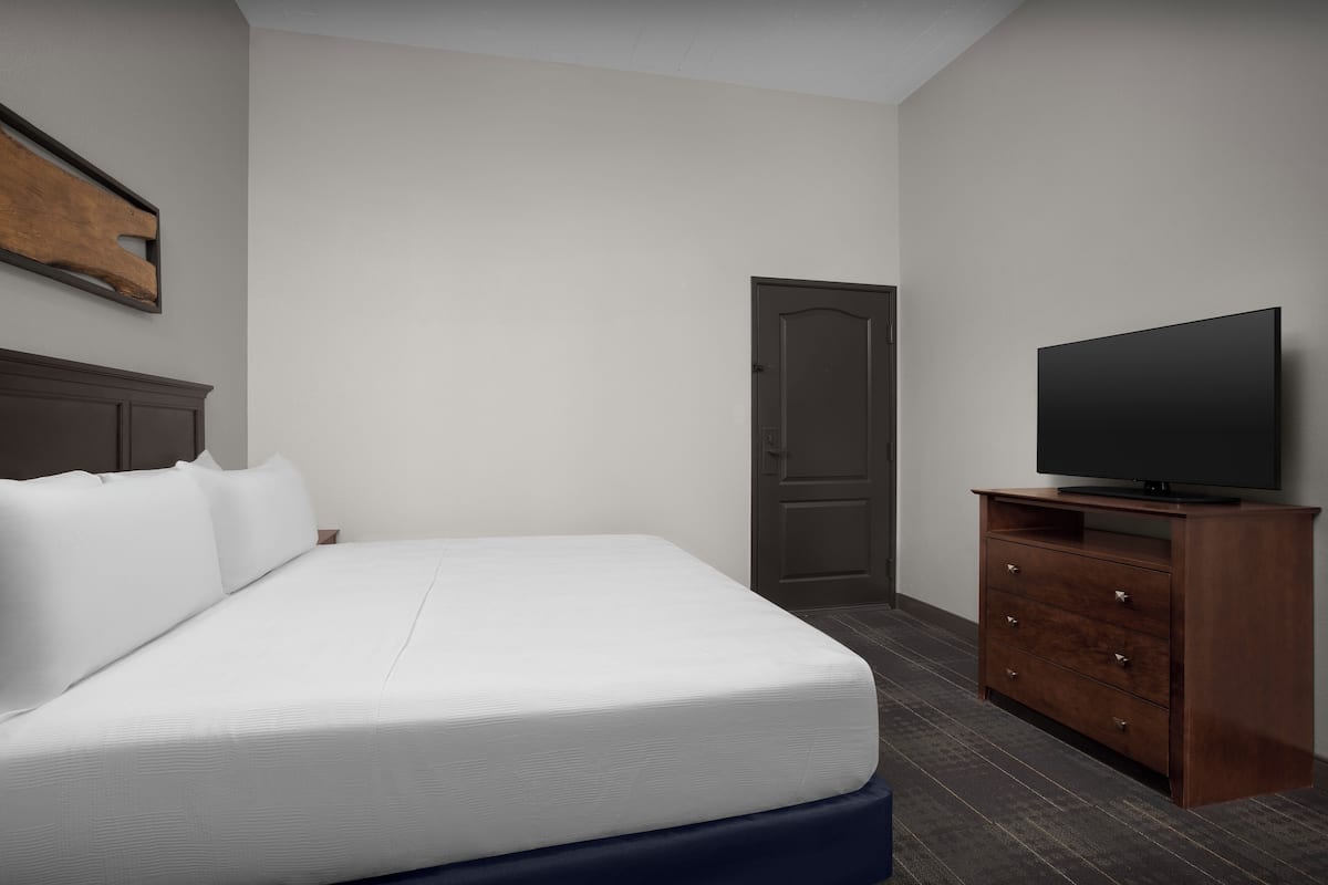 A hotel room with a bed, a wooden dresser, a television, and a door.