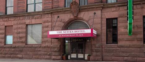 The Suites Hotel at Waterfront Plaza with a brick facade, large arched entrance, and a prominent sign.