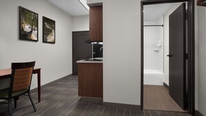 Una cocina moderna con estufa integrada, un rincón comedor con una silla y un acceso a un baño.