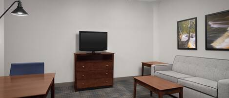 A modern living room with a flat-screen TV on a wooden stand, a grey sofa, a coffee table, a blue chair, and a patterned carpet.