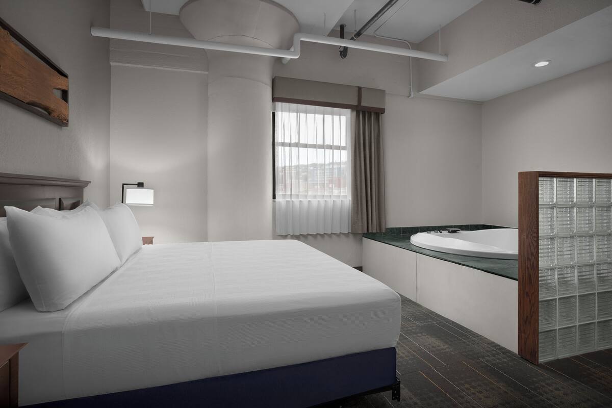 A modern hotel room with a large bed, a bathroom with a glass shower enclosure, and a view of the city through the window.