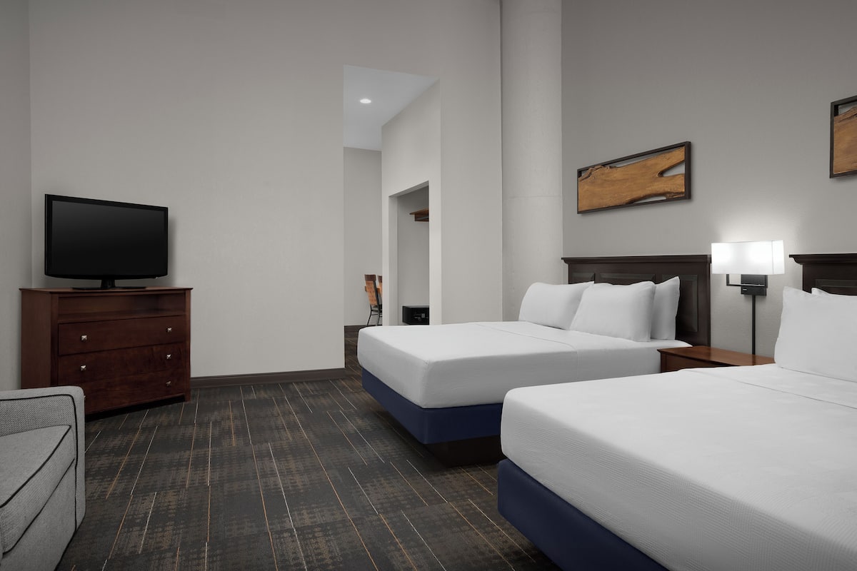 A hotel room with two beds, a TV on a dresser, and a painting on the wall.