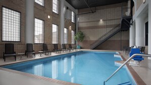 Una piscina interior con suelo de baldosas, una escalera y zonas de estar con sillas y mesas.