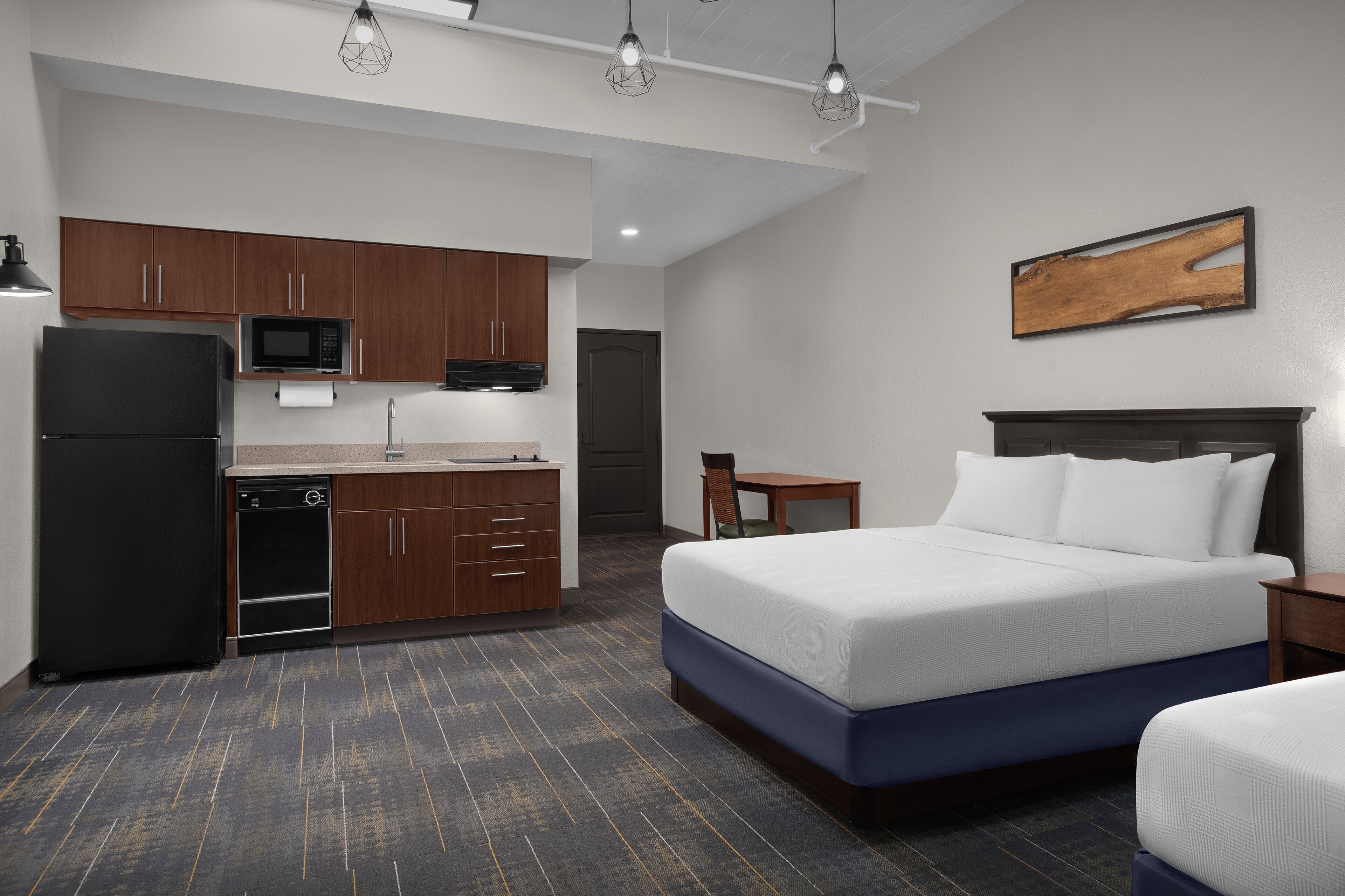 A hotel room with a bed, a small desk, a microwave, and a refrigerator.
