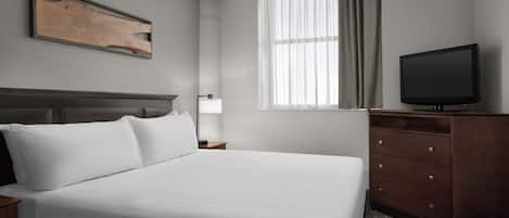 Ein Hotelzimmer mit einem großen Bett, einem Flachbildfernseher, einem Holzkopfende, einem Fenster mit Vorhängen und einer Holzkommode.