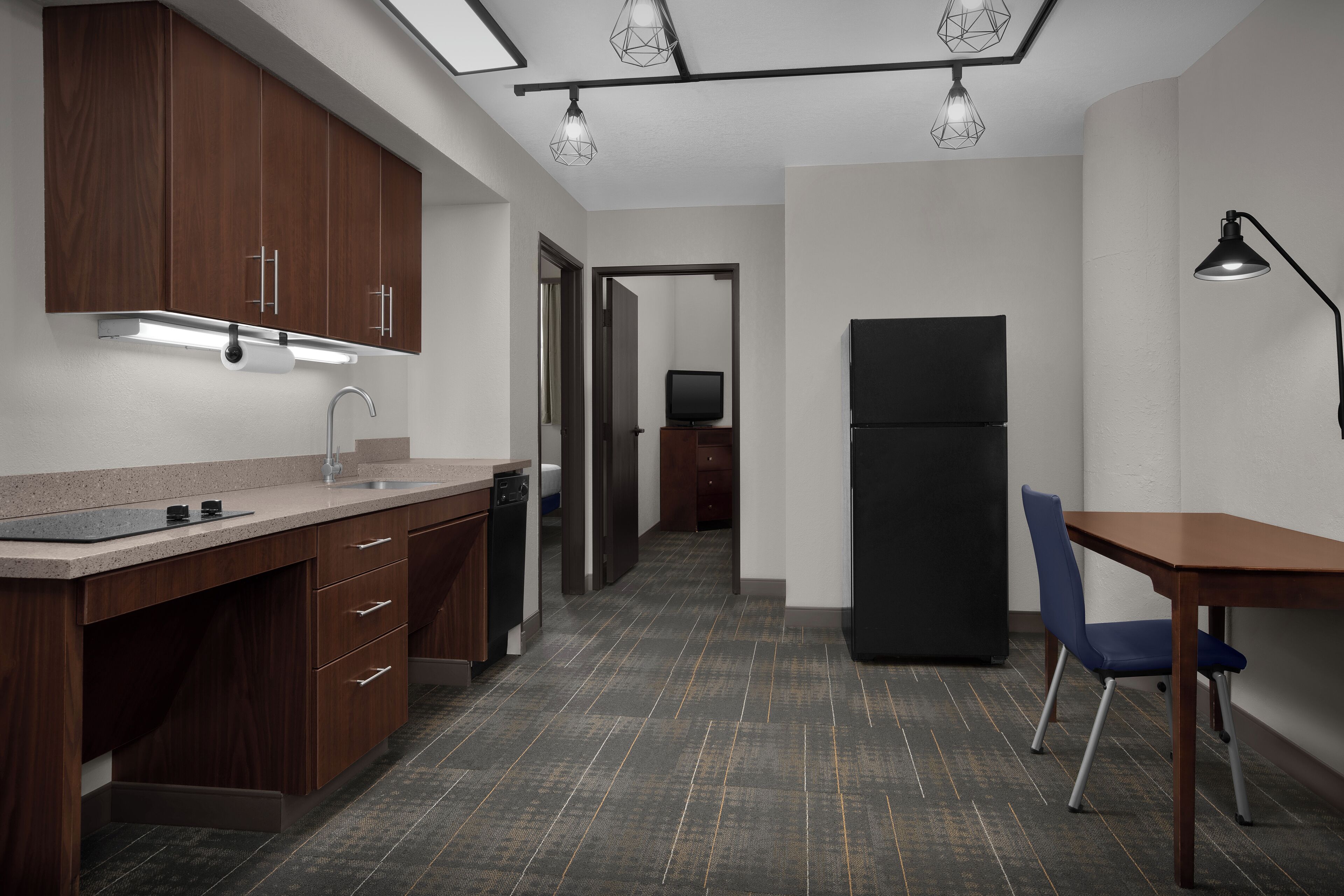 A modern kitchen with wooden cabinets, a countertop, a sink, and a dining area with a table and chair.