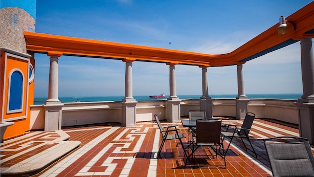 Una terraza al aire libre con suelo estampado, columnas blancas y barandillas anaranjadas.