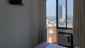 Habitación de hotel con cama, televisor montado en la pared, ventana grande con vista a la ciudad y aire acondicionado.