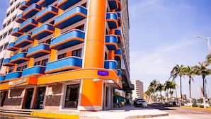 Un hotel de varios pisos con balcones, un llamativo esquema de color naranja y azul, y cielo despejado.