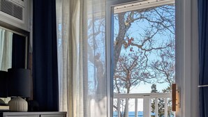 A bedroom with a bed, a desk, a chair, a window with a view of trees and a body of water. - Ocean View Terrace Inn (Hampton Bays)