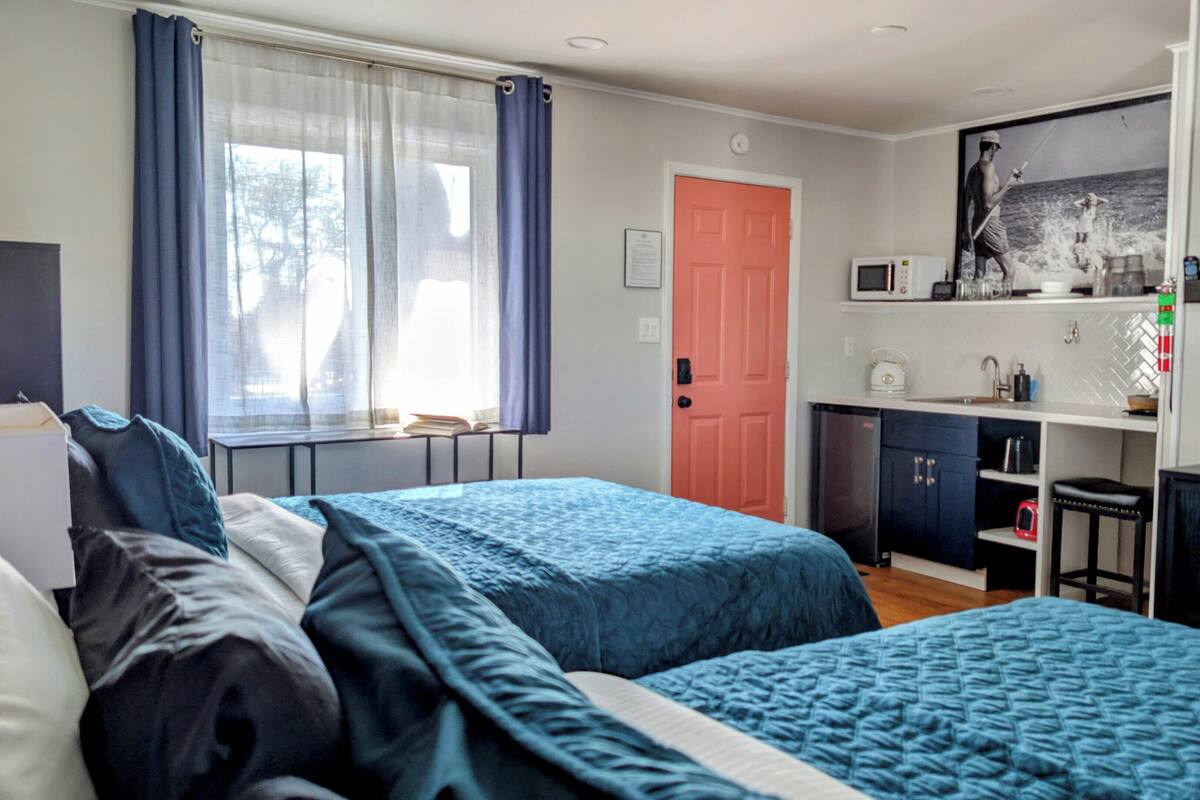 Habitación de hotel con dos camas, kitchenette, televisor y ventana con cortinas.