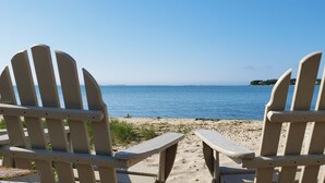 Two Adirondack chairs facing a beach with a clear view of the sea and a distant island. - Ocean View Terrace Inn (Hampton Bays)