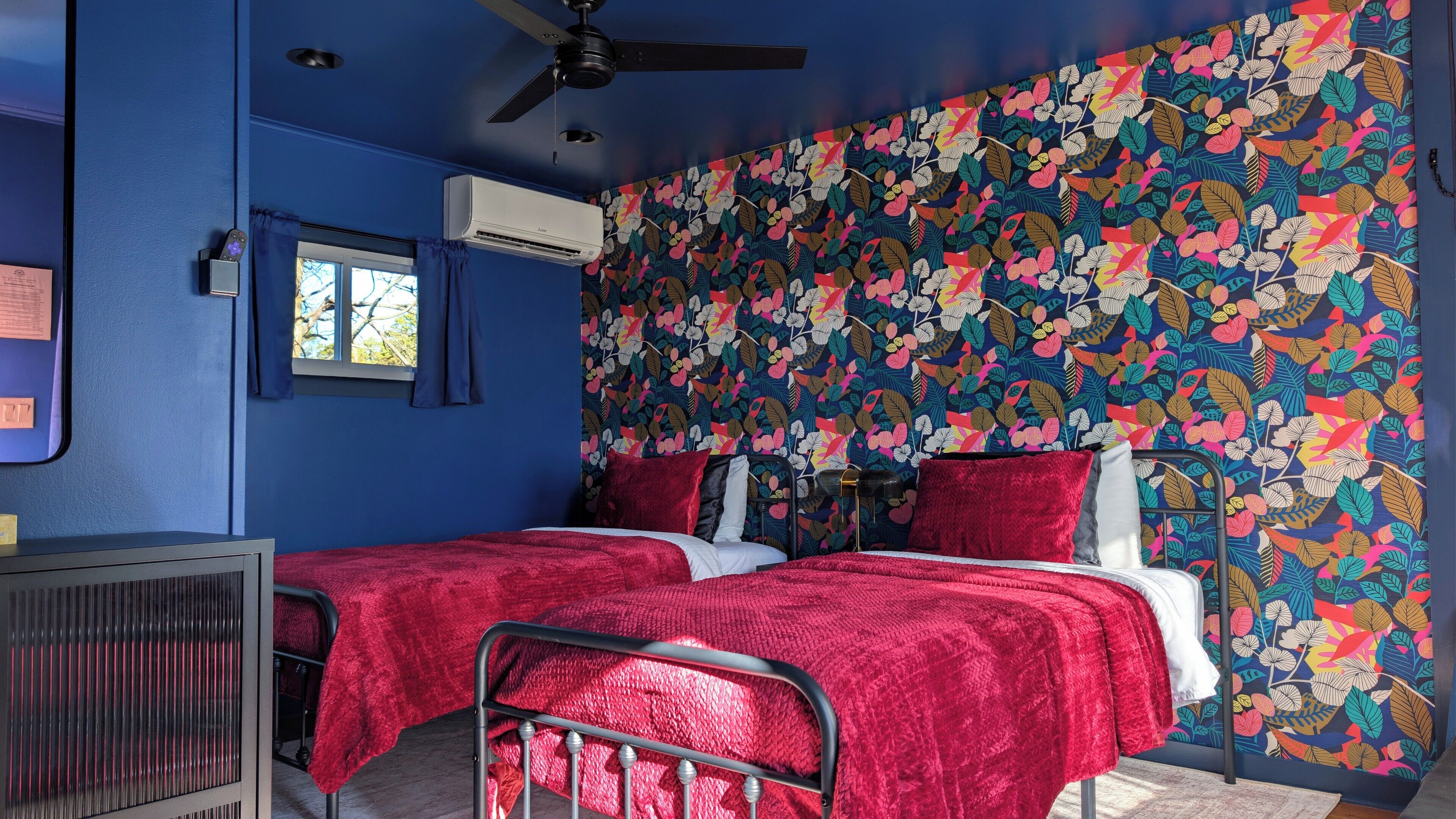Une chambre avec deux lits, un ventilateur de plafond, un appareil de climatisation et une fenêtre avec des rideaux.