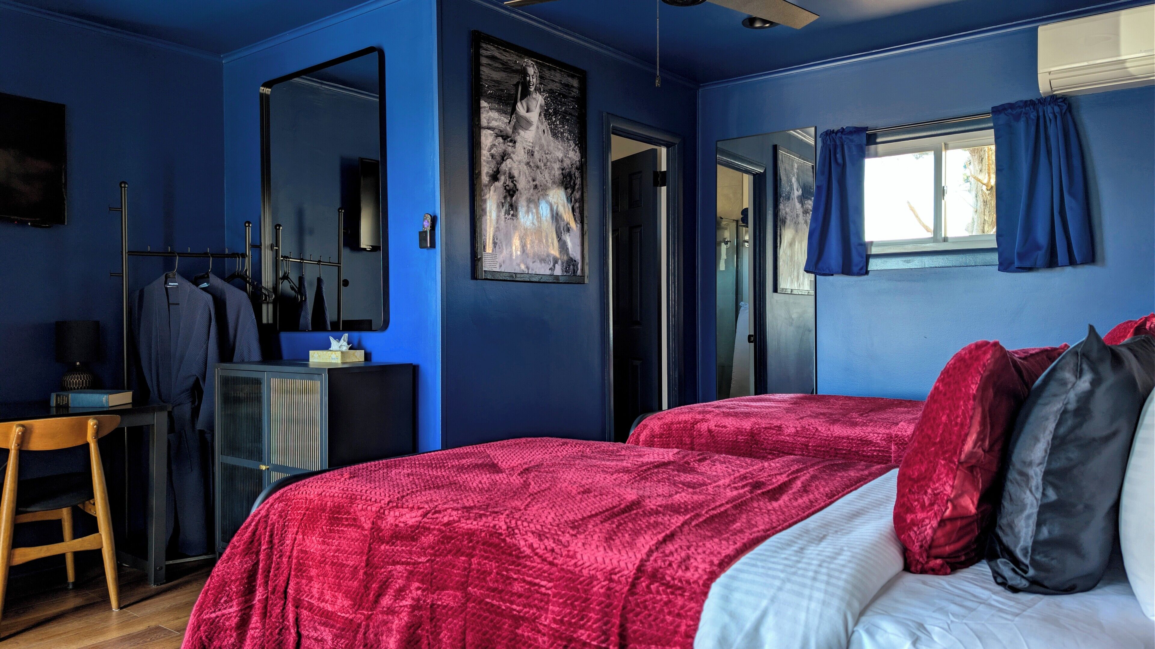 A room with two beds, a desk, a mirror, and a door leading to another room.