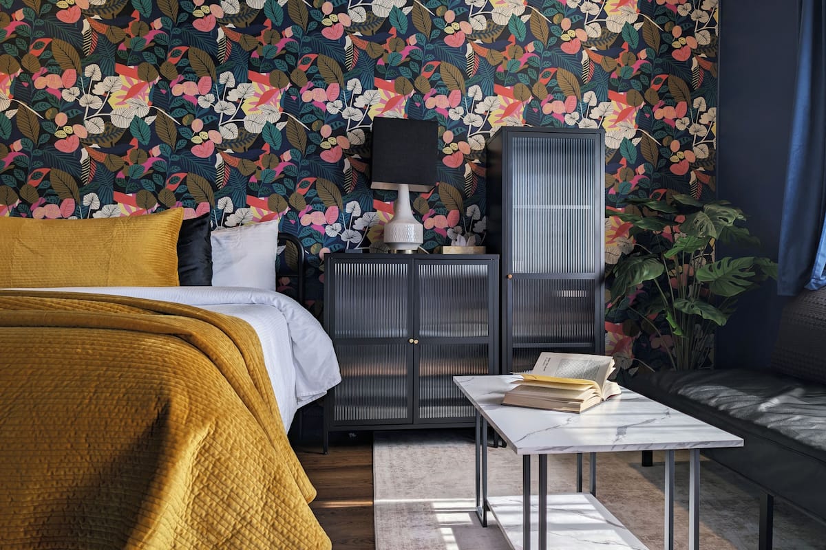Un dormitorio con cama, mesita de noche, mesa, sofá, armario y ventana con cortinas.