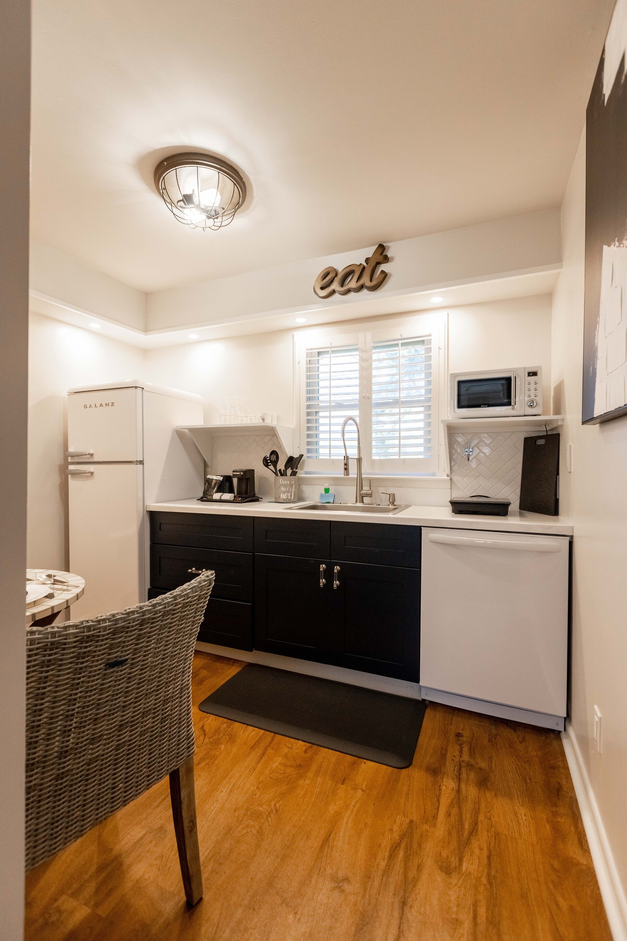 A compact kitchen with a refrigerator, microwave, sink, and a dining area with a chair.