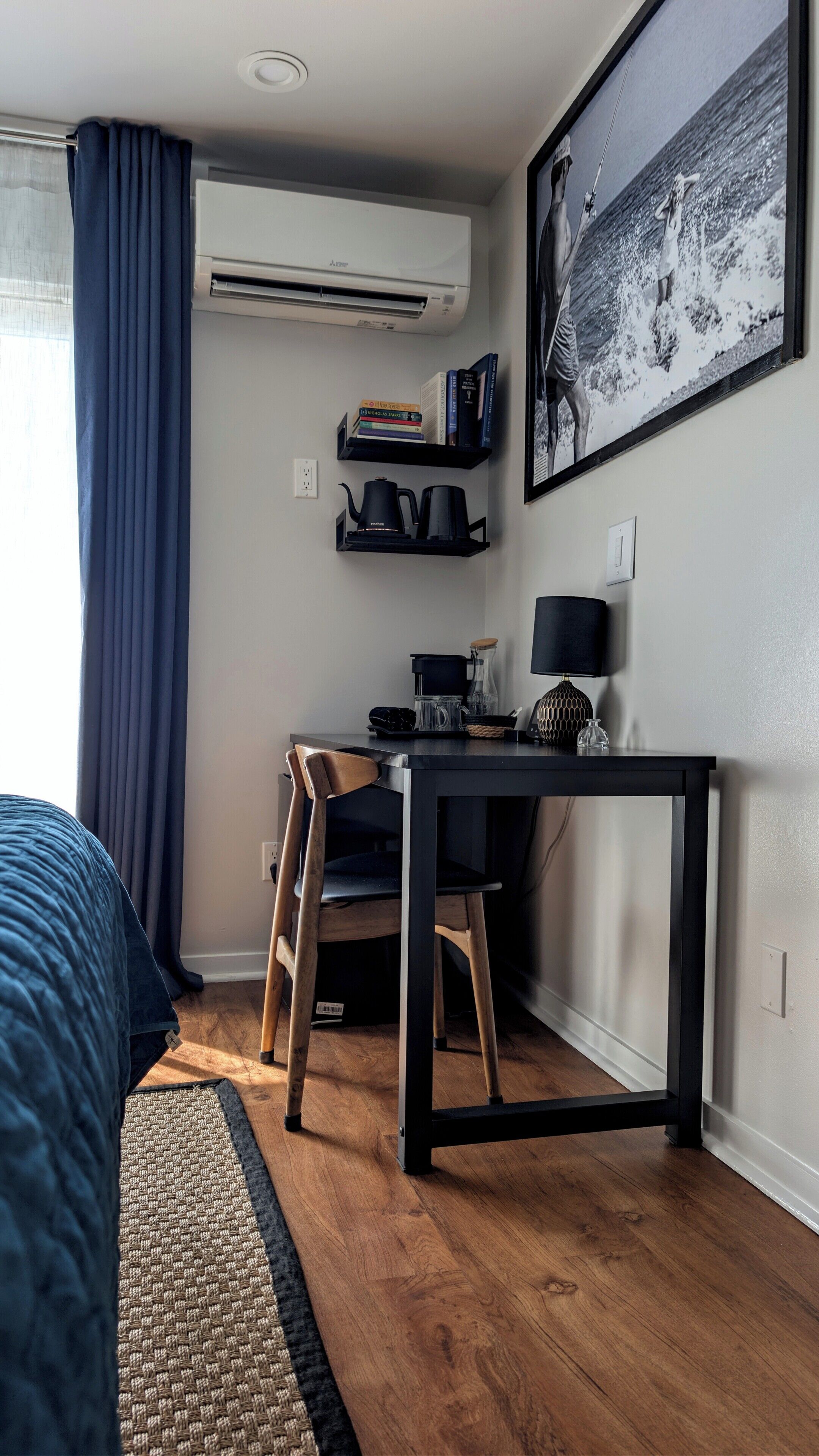 A room with a bed, a desk with a chair, a coffee maker, a lamp, and a wall-mounted air conditioner.