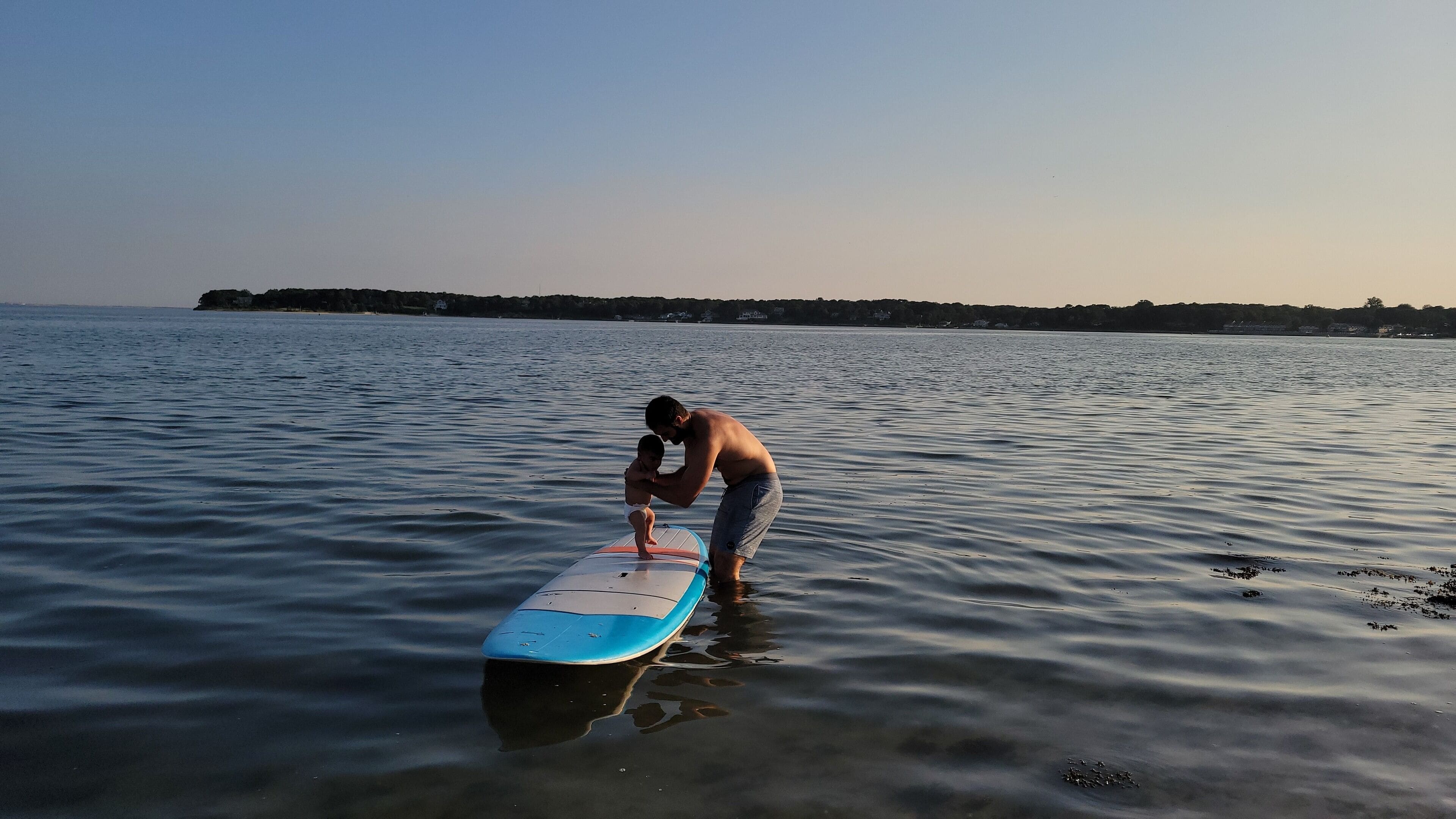 En mand står i roligt vand med et surfbræt.