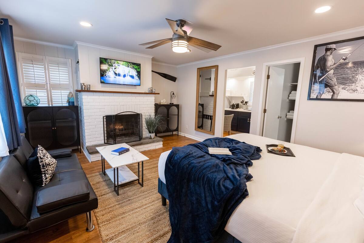 Una sala de estar moderna con chimenea, ventilador de techo, televisor y cama.