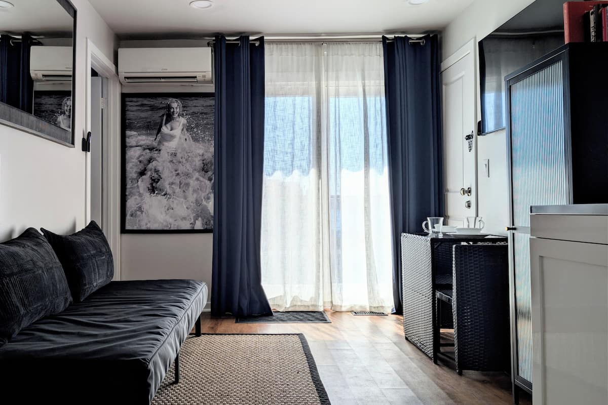 Una habitación moderna con sofá, lámpara, un cuadro abstracto grande, ventana con cortinas y un radiador.