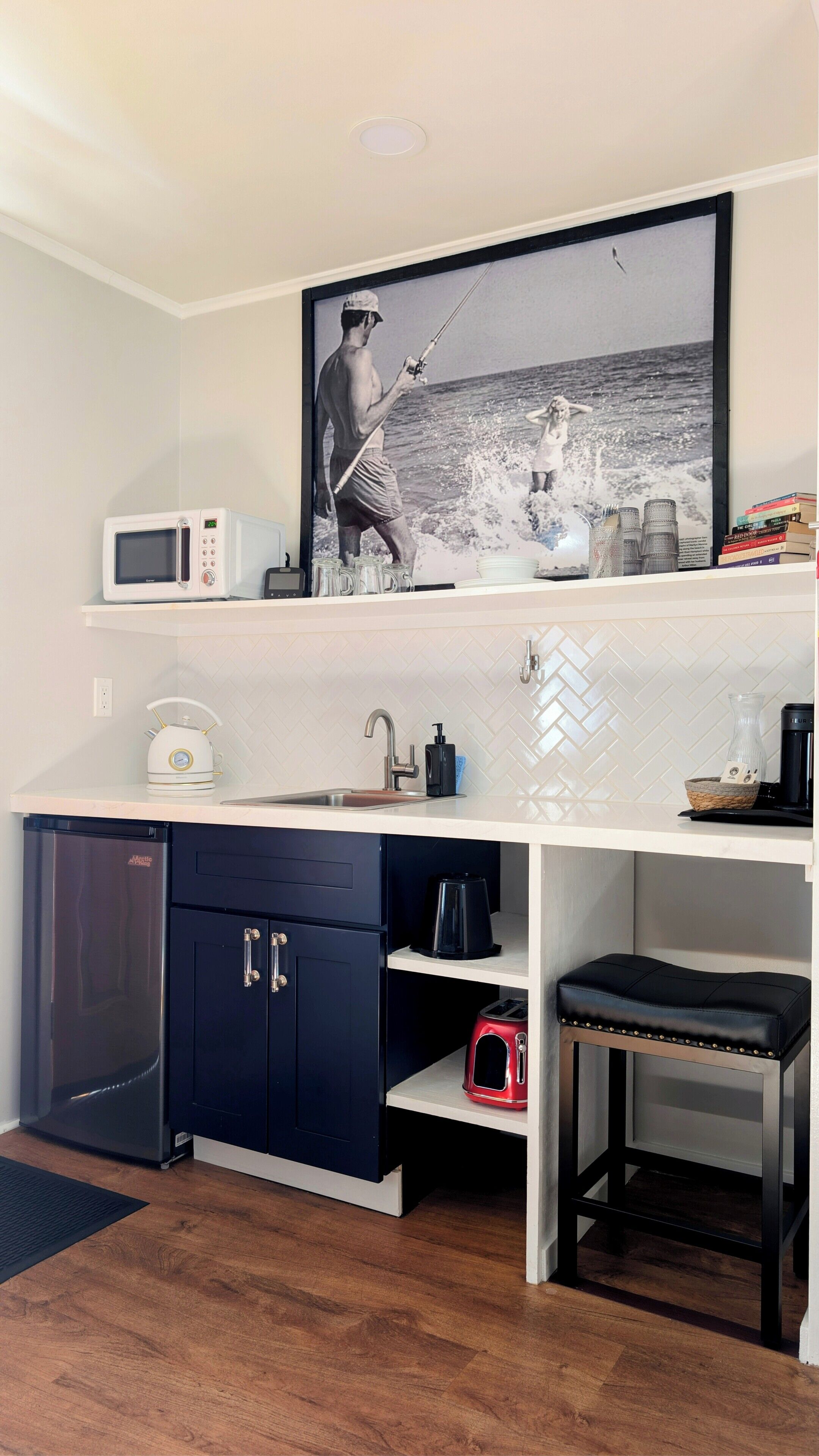 A compact kitchen with a microwave, kettle, sink, and a small refrigerator.
