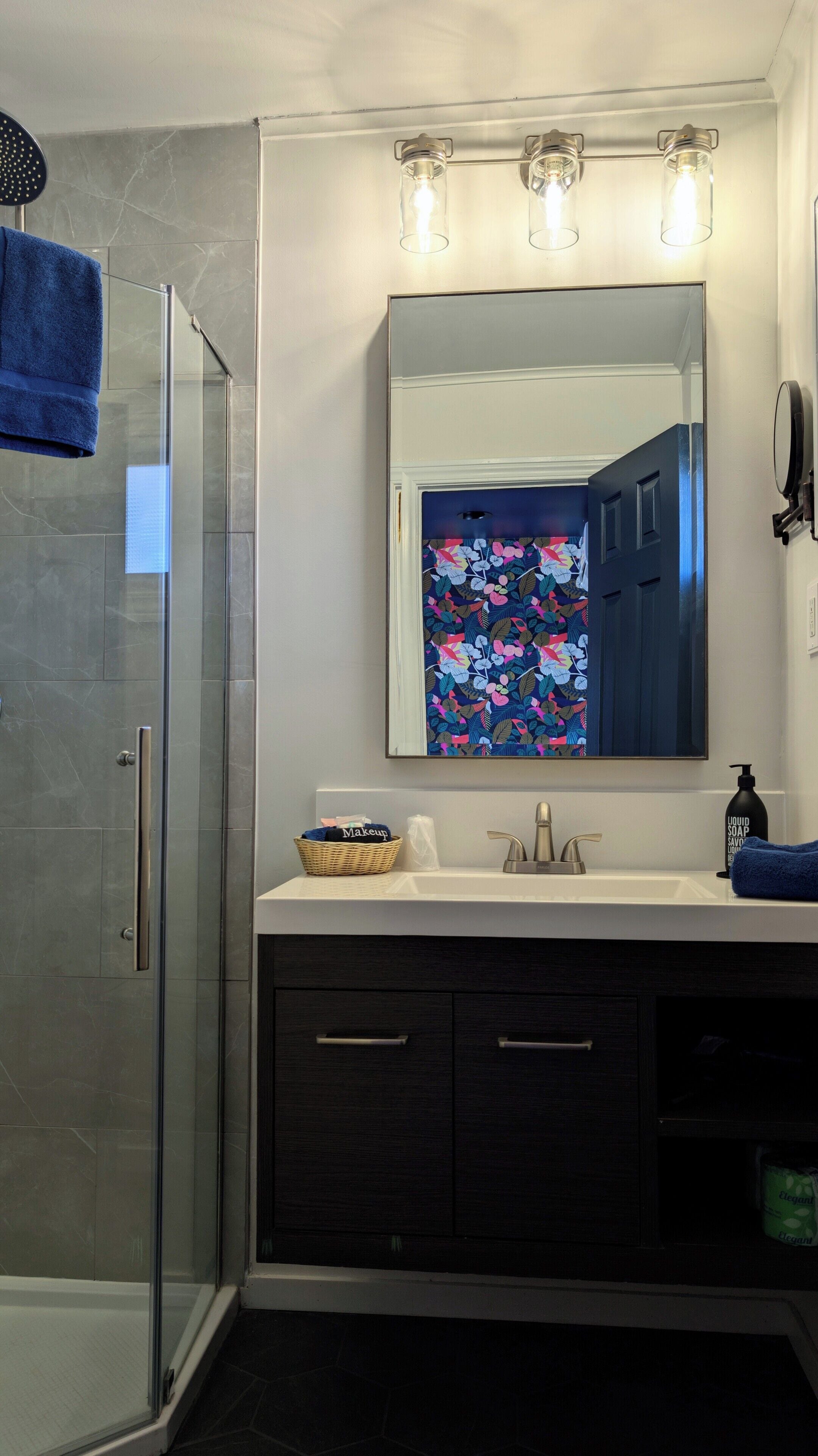 Un bagno con box doccia in vetro, un lavabo con specchio e un'opera d'arte floreale sopra lo specchio.