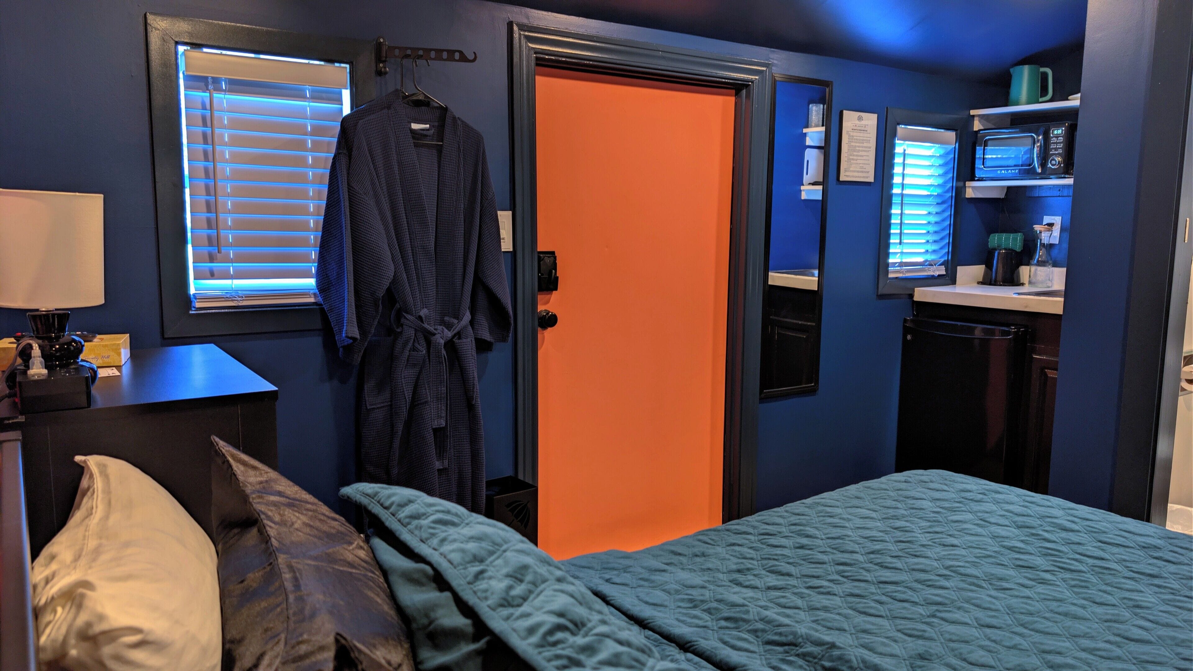 Quarto com cama, roupão pendurado em um gancho, micro-ondas e cafeteira no balcão.