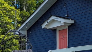 A house with a dark blue exterior, a white porch railing, and a red door. - Ocean View Terrace Inn (Hampton Bays)