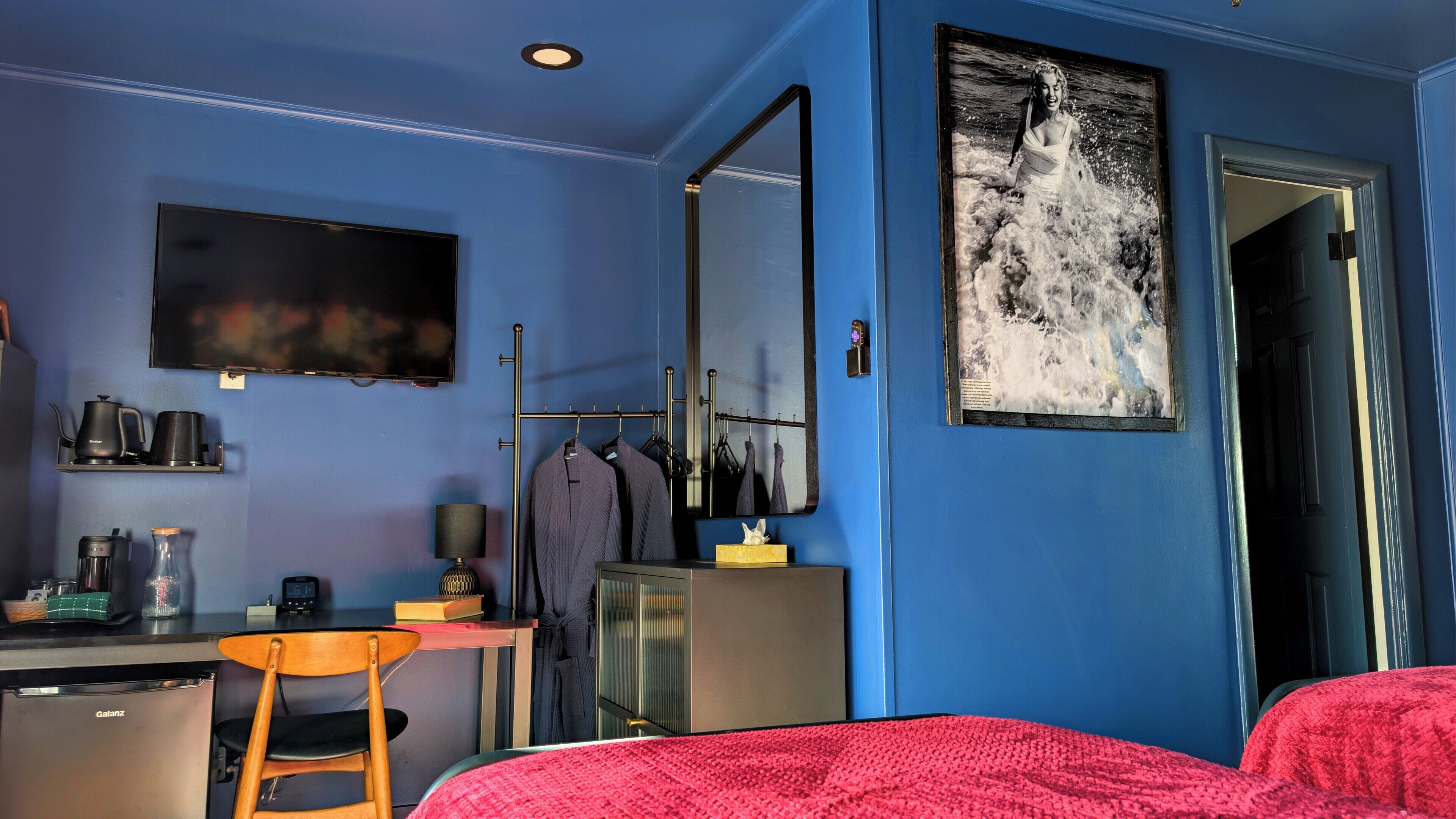 Une chambre comprenant un lit, un bureau, une chaise, une télévision, un miroir et une machine à café.