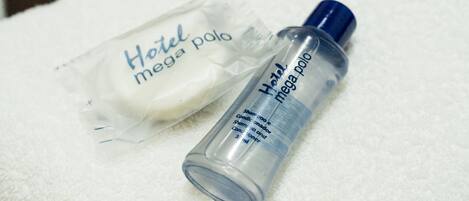 A bathroom with a white towel, a bottle of Hotel mega polo shampoo, and several bottles of shampoo in the background.