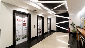 A modern hotel lobby with a polished floor, three elevator doors, and a reception desk with a plant. - Hotel Mega Polo (São Paulo)