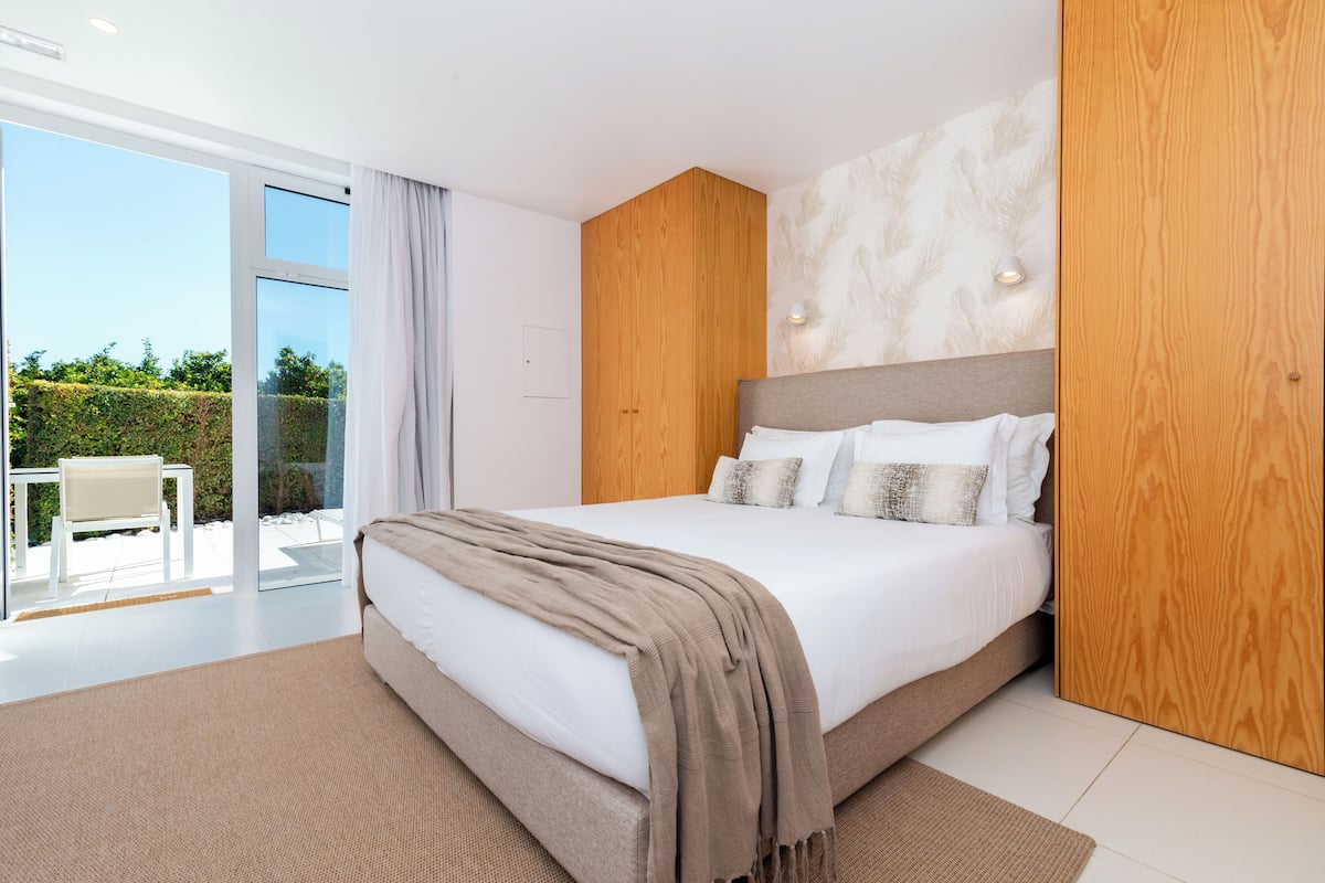 Une chambre moderne avec un grand lit, un lambris en bois et une vue sur l’extérieur.
