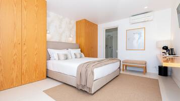 A modern bedroom with a large bed, a wooden wardrobe, a bench, and a bathroom visible through an open door.